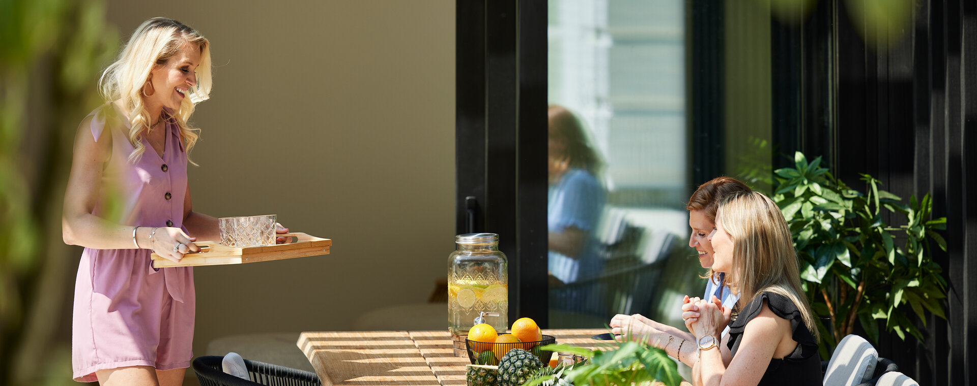 Drei Frauen bereiten unter halb geöffneten Lamellendach Cocktails zu